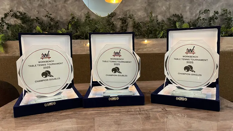 Three WorkBench Table Tennis Tournament 2025 champion plaques in open cases