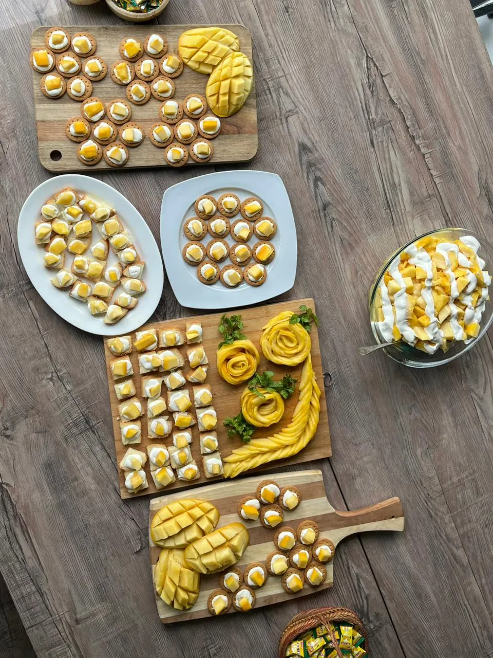 Mango canapes laid out on wooden boards and white plates at WorkBench, photographed from above, with carved mango roses, sliced mango and a glass bowl of mango and cream.