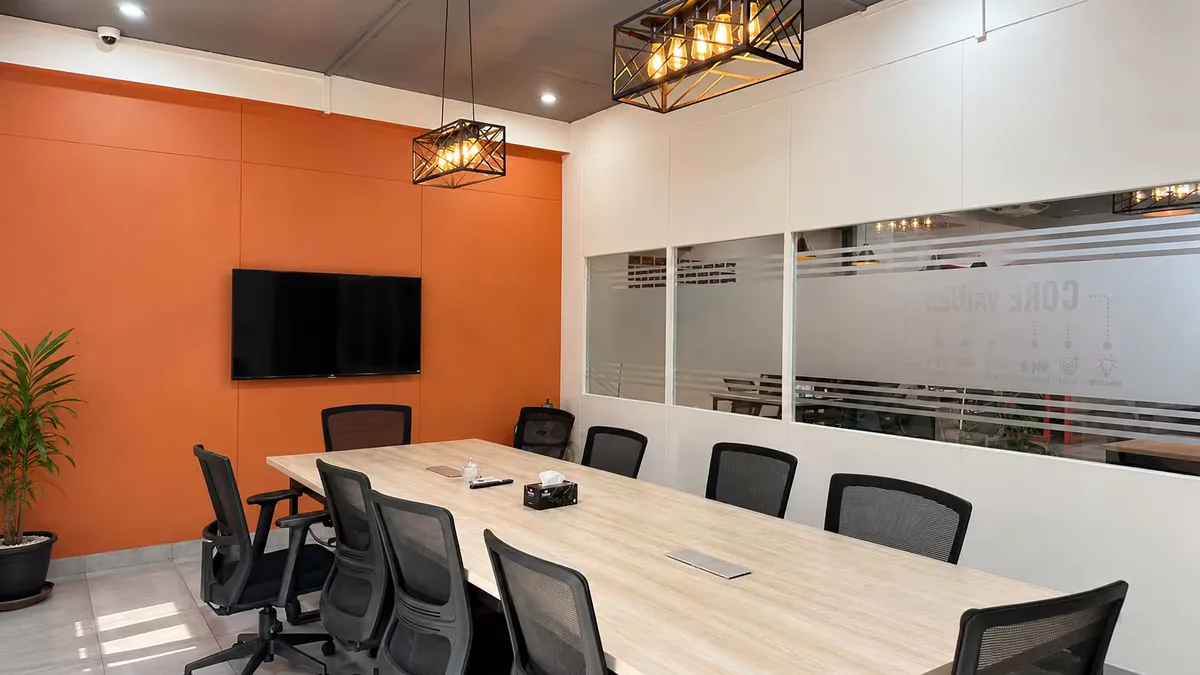 The meeting room at WorkBench from the other end: the long table facing a wall-mounted screen on the terracotta panelled wall, with the Core Values wall showing through a frosted glass partition.