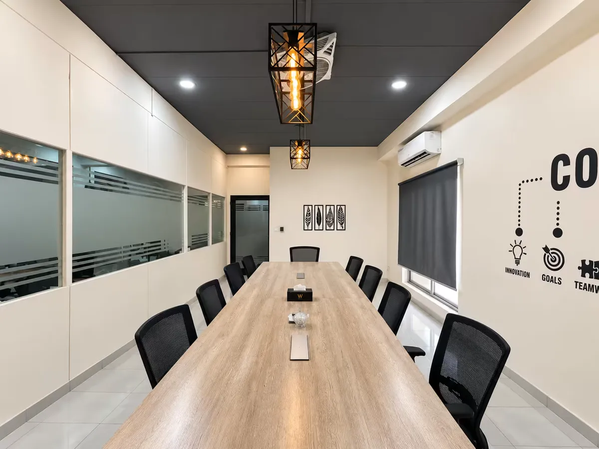 The meeting room at WorkBench, looking down the long light wood table under geometric cage pendant lights, with the Core Values lettering on the wall to the right and a frosted glass partition on the left.
