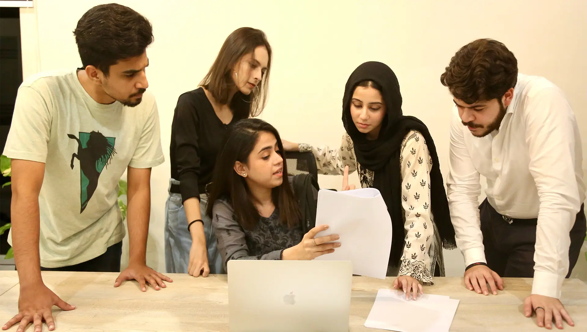 Five members gathered around a laptop and papers at a table