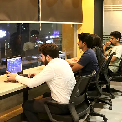 Four members working at the window counter at WorkBench after dark, with lit shop signs in the street outside the glass.