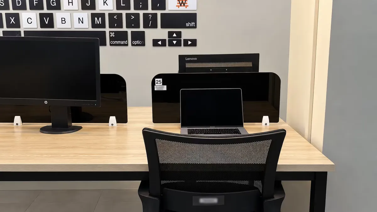 A dedicated desk at WorkBench, numbered and reserved, with a monitor, a laptop and black privacy dividers on either side