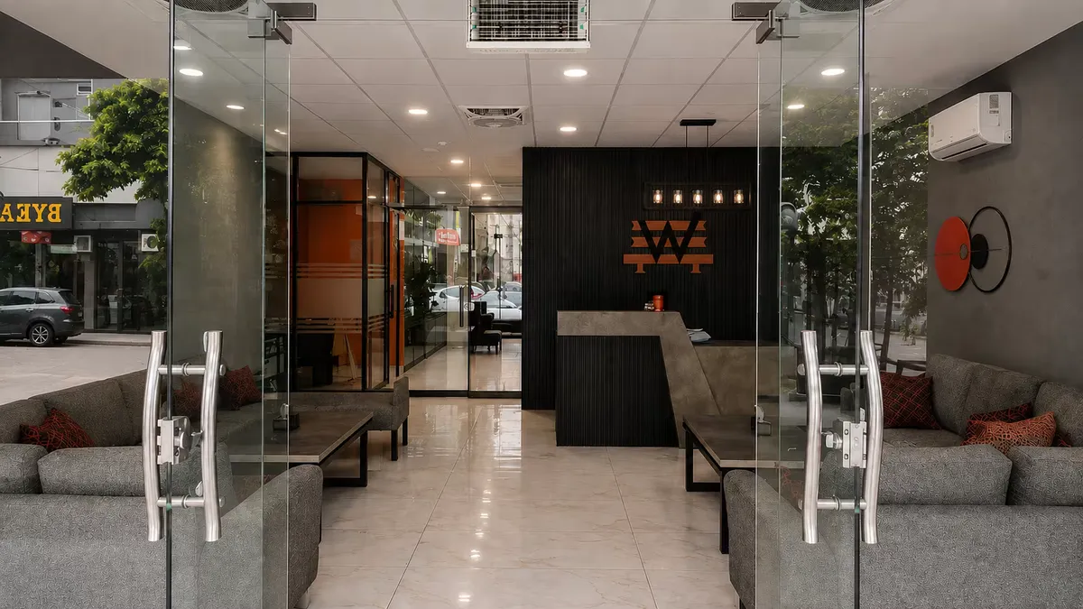 The glass street entrance to WorkBench in Valencia Town, Lahore, looking through the doors to the reception desk and the amber W on the charcoal fluted wall.