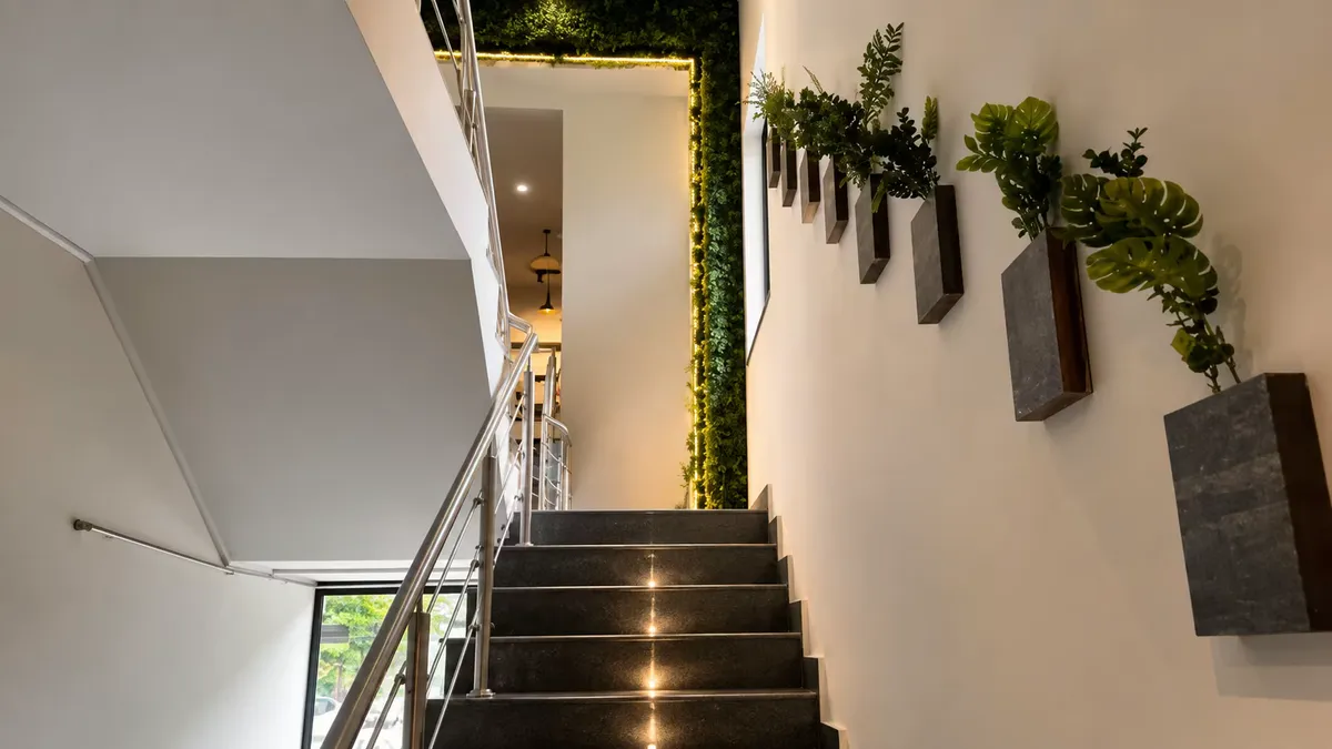 The staircase at WorkBench: dark stone treads with a steel handrail, wall-mounted planters climbing the side wall and a moss-covered archway lit warm at the top.